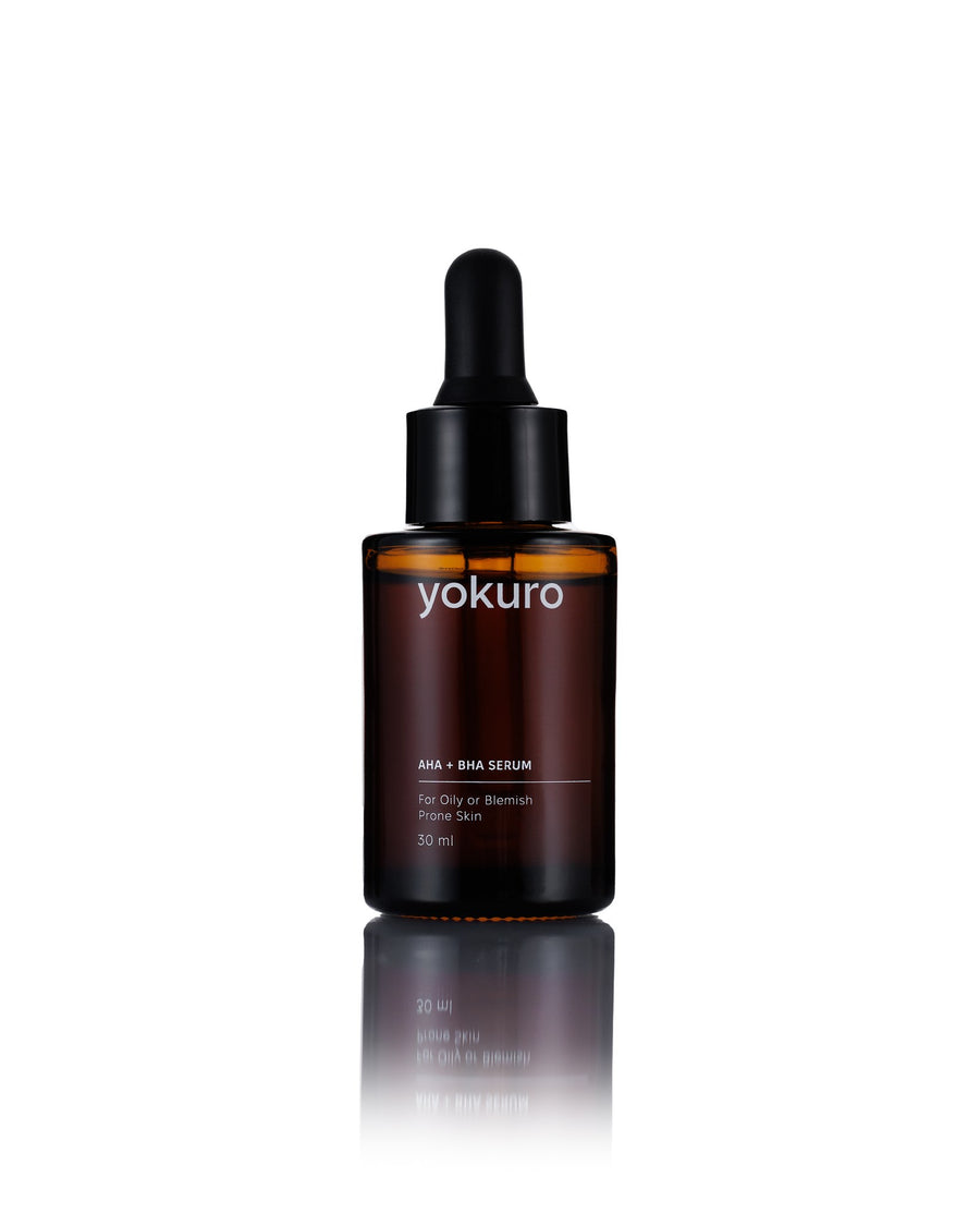 A 30 ml amber glass dropper bottle of yokuro AHA + BHA SERUM on a white background with a soft reflection below.
