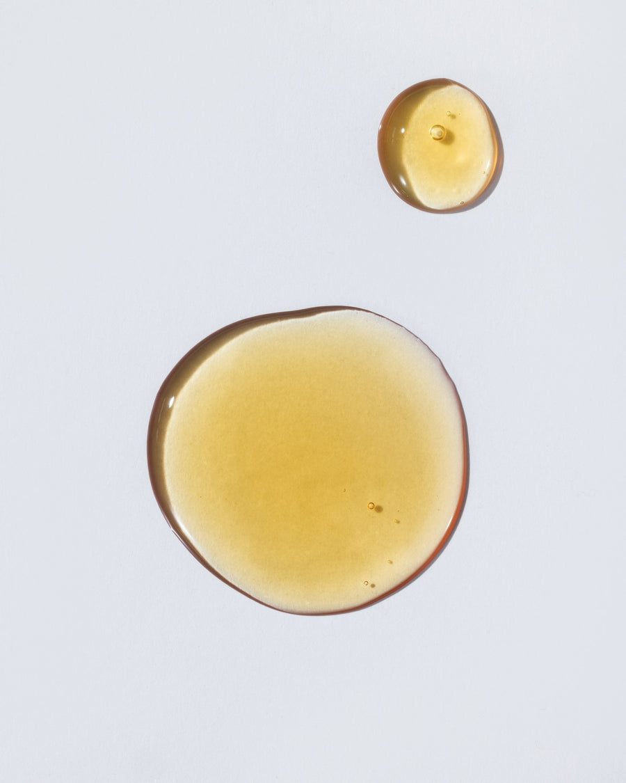 Two translucent golden-yellow liquid droplets on a plain light gray background.