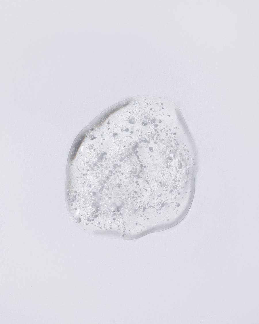 A single clear, translucent gel or liquid droplet with fine bubbles, centered on a plain light gray background.