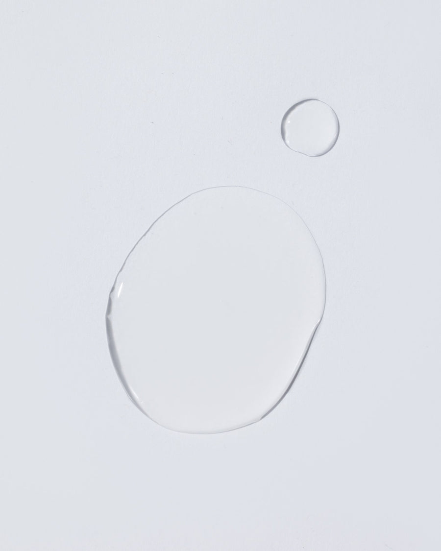 A clear, transparent liquid droplet with a large oval shape and a smaller circular droplet on a plain light gray background.
