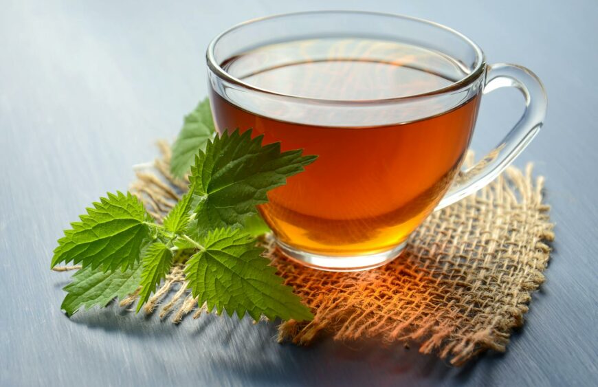 A close-up of herbal tea in a glass cup with fresh mint leaves on a table.